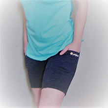 Load image into Gallery viewer, Grey black heather bike shorts on a model. High waisted and the hands are in the pockets to  show the size. The length of the shorts is mid thigh.