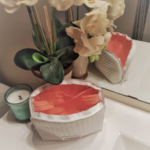 makeup bag with coral lining. flowers behind the open bag on the bathroom sink edge.