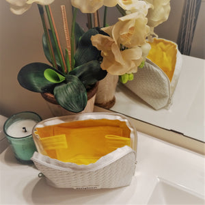 yellow bamboo/cotton lined makeup bag sitting on a sink. flowers and a chandler in background.