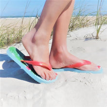 Load image into Gallery viewer, Someone's feet in flip flops on the sand.