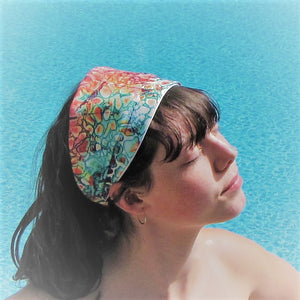Young lady sitting on the edge of the pool. She has a headband in jewel tones, looks like water spots